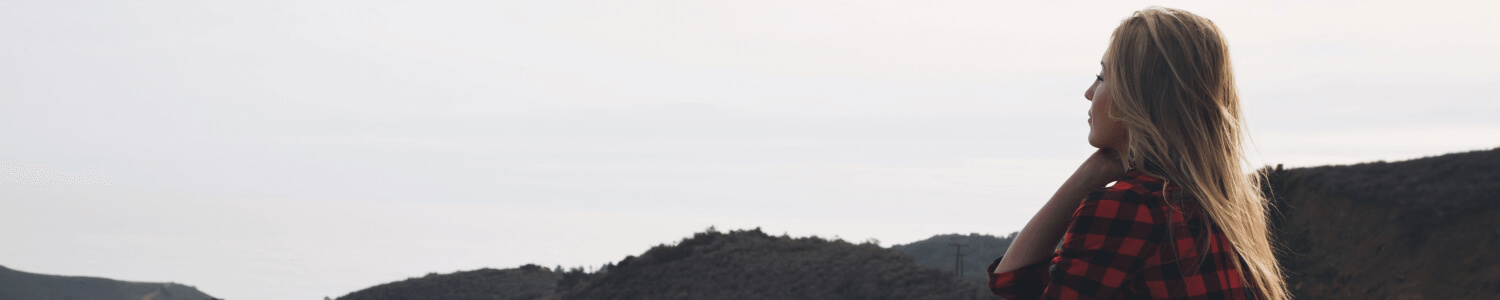 Woman sitting on bonnet of car overlooking hills